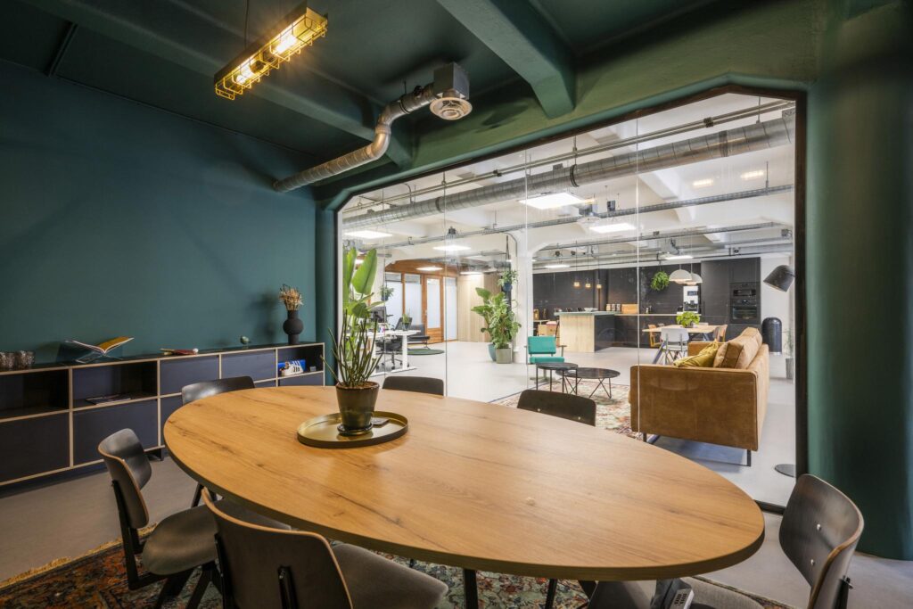 Modern meeting room with a wooden table and plant, overlooking a stylish open office space on Van Diemenstraat.